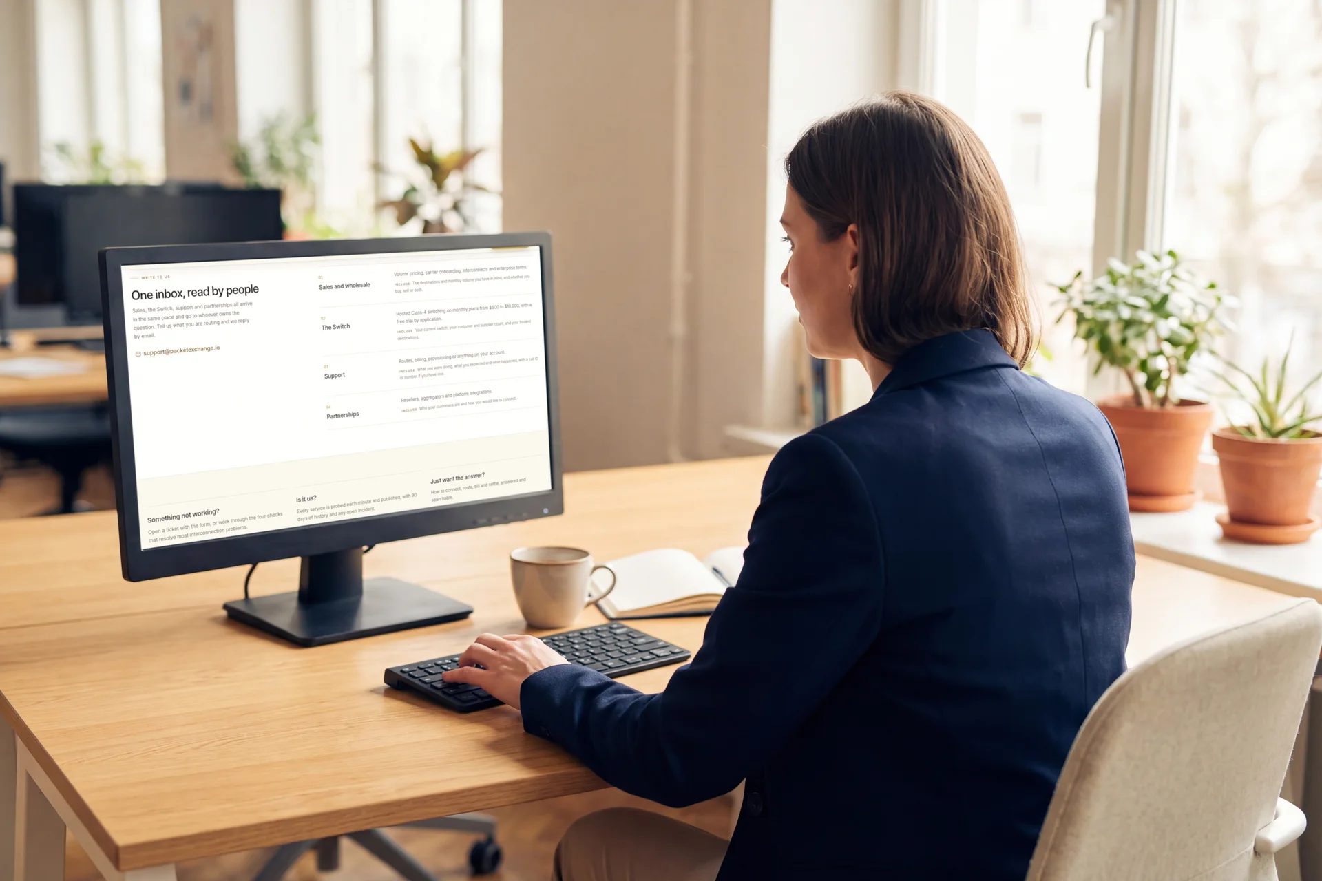 A commercial manager at her desk reading the PacketExchange contact page, its enquiry topics on her monitor